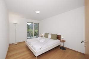 a white bedroom with a bed and a window at Chasa Miramunt 2 in Scuol