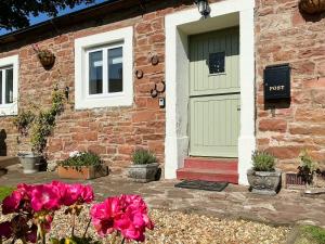 a brick house with a green door and pink flowers at Abbey Cottage in St Bees