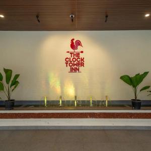 a sign for the clock tower inn on a wall with plants at The Clock Tower Inn in Bangalore +3 photos
