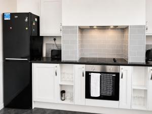 a kitchen with a black refrigerator and white cabinets at Cinderhouse Highbury Vale in Nottingham