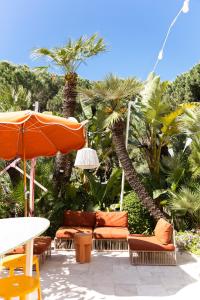 a patio with chairs and an umbrella and palm trees at Hôtel Juana in Juan-les-Pins