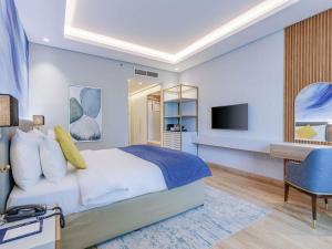 a bedroom with a bed and a desk and a television at Mövenpick Grand Al Bustan in Dubai