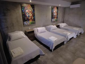 three beds in a room with paintings on the wall at El Norte Hotel in Río Segundo