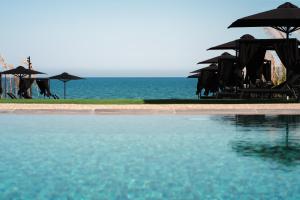 a swimming pool with umbrellas and the ocean at NOE Suites in Ayios Theodhoros