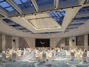 a ballroom with tables and white chairs and a stage at Movenpick by Accor Qingdao Sunmei in Qingdao