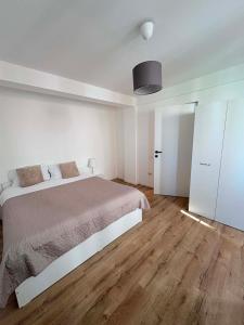 a white bedroom with a large bed and wooden floors at The Urban Nest apartament in Giurgiu