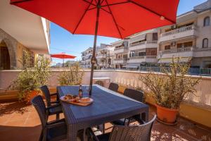 a table and chairs with a red umbrella on a balcony at Apartamentos Obelisc in Can Picafort