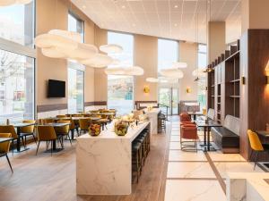 a restaurant with tables and chairs and large windows at Mercure Achères St Germain en Laye in Achères