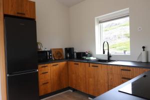 a kitchen with wooden cabinets and a black refrigerator at Hvammur 10 with private hot tub in Kaldrananes +13 photos