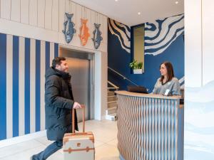a man walking past a woman with a suitcase at ibis Styles Bordeaux Lac Bruges in Bordeaux +131 photos