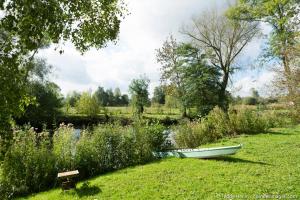 a small boat sitting in the grass next to a pond at La Bulle au bord de l'eau in Épagne-Épagnette