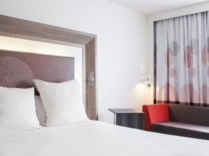 a hotel room with a bed and a red chair at Novotel Nottingham Derby in Long Eaton