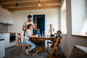 a man and two children sitting at a table in a kitchen at Maison d hôtes Les Bruyères in Bonvillars +11 photos