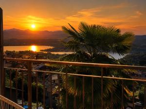 a sunset from a balcony with a palm tree at Panorama - Lake Maggiore House in Colazza