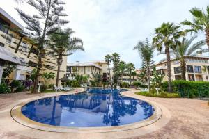 a large swimming pool with palm trees and buildings at Spacious apartment, pool, beach, basement parking in Bouznika