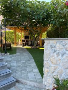 a garden with a stone wall and a tree at Legacy apartment 1 with privat jacuzzi and apartment 2 with BBQ in Novalja