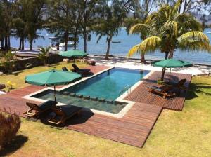 a swimming pool with chairs and umbrellas next to the water at Olana Beachfront Apartments in Rivière Noire