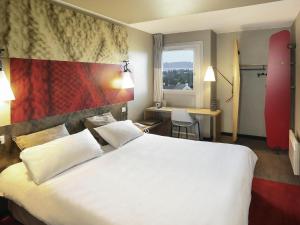 a hotel room with a large white bed and a desk at ibis Saint Brieuc Yffiniac in Yffiniac