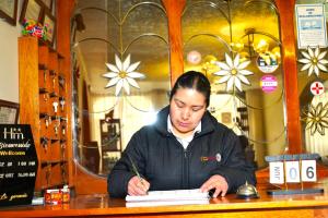 a woman sitting at a table writing on a book at Hotel Margarita in Puno