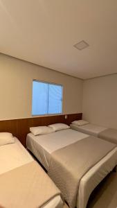 three beds in a room with a window at Pousada Bella in Vitória da Conquista