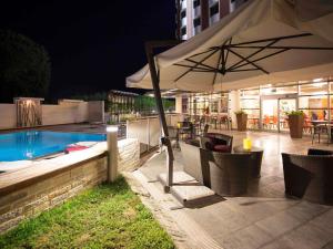a patio with an umbrella next to a swimming pool at Novotel Salerno Est Arechi in Salerno