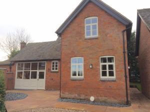 a brick house with white windows and a driveway at Woodleighton Cottages in Uttoxeter
