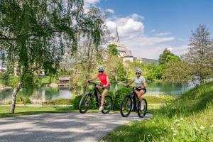 two people riding bikes down a road near a lake at Reed by Linde in Maria Wörth
