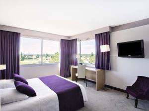 a hotel room with a bed and a desk and window at Mercure Toulouse Aéroport Golf de Seilh in Seilh