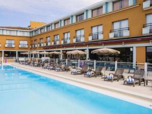 a hotel with a swimming pool and chairs and umbrellas at Mercure Toulouse Aéroport Golf de Seilh in Seilh