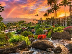 a rainbow over a garden with flowers and palm trees at NEW Sunset Hideaway with Beach Access Pools & AC in Princeville