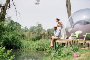 a man and a woman sitting on a dock fishing at La Bulle au bord de l'eau in Épagne-Épagnette