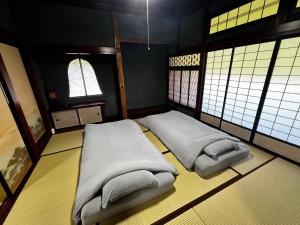 two beds in a small room with windows at 一棟貸し古民家赤ちゃんから楽しめる文化庁選定重要伝統的建造物 築130年"古民家ゆうなぎ"小松空港から35分 金沢から60分 in Kaga +44 photos