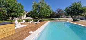 a swimming pool with chairs and a wooden deck at La Romantique du Château in Gaillan-en-Médoc
