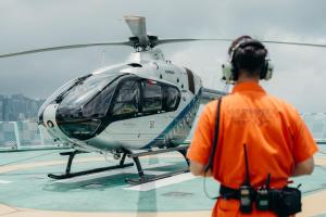 a man in an orange shirt standing next to a helicopter at The Peninsula Hong Kong in Hong Kong