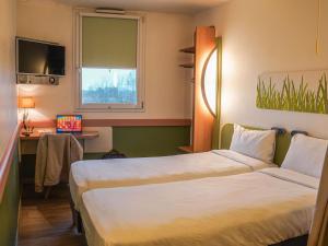 a hotel room with two beds and a desk and a window at Ibis Budget Bayeux in Bayeux