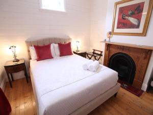 a bedroom with a white bed with red pillows and a fireplace at Poets Cottage c1912 Scenic Hikes, Fire, Spa Bath in Wentworth Falls