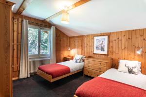 two beds in a room with wooden walls and a window at Mont Gele Hotel in Verbier