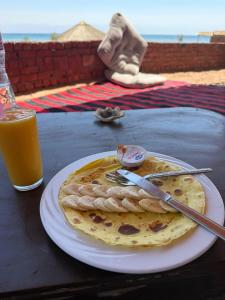 a plate with two pancakes on a table with a glass of orange juice at Marhaba Camp in Nuweiba