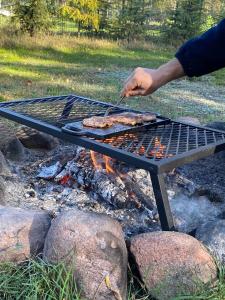 Eine Person bereitet Essen auf einem Grill zu. in der Unterkunft Wrzosowisko - Leśny Azyl dla Dwojga in Smolarnia