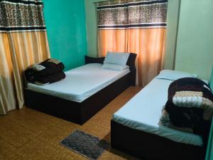 two beds in a room with green walls and curtains at Ilam Pahuna Ghar in Ilām