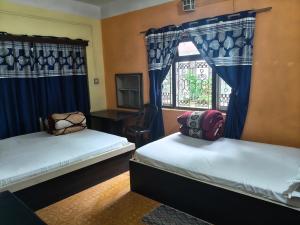 two beds in a room with blue curtains and a window at Ilam Pahuna Ghar in Ilām
