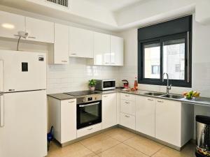 a white kitchen with white appliances and a window at Mamad Family Friendly New Condo By Feelhome in Yerushalayim