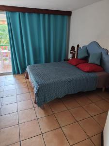 a bedroom with a bed with blue curtains and a tile floor at Studio Hibiscus in Sainte-Anne