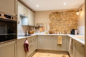 a kitchen with white cabinets and a stone wall at Beechwood Cottage | Banham Cottages in Bourton on the Water +27 photos