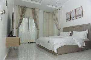 ein weißes Schlafzimmer mit einem großen Bett und einem Fernseher in der Unterkunft White Pole Apartments in Abuja