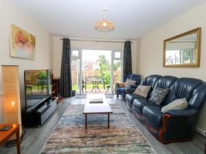 a living room with a leather couch and a tv at The Mill House Gardens in Lowestoft
