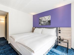 a bed in a hotel room with a purple wall at Mercure Lenzburg Krone in Lenzburg +82 photos