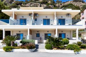 a large white building with blue windows and bushes at Skinos Apartments in Plakias