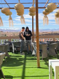 two men standing under a pergola with tables and chairs at Qamar Mgouna Hotel in El Kelaa des Mgouna