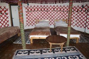 a room with three beds and a table and a stool at Happy Nomads - Modern Yurt Cottages & Breakfast in Karakol